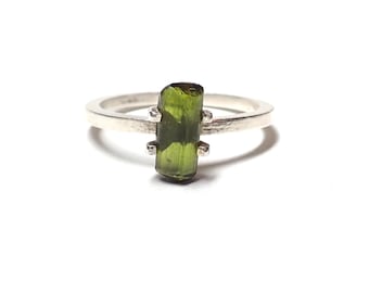 May include: A silver ring with a green gemstone. The gemstone is a rectangular shape and has a rough, natural look.