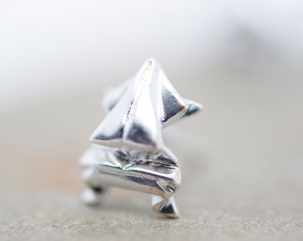 May include: A silver origami sailboat charm, a small, detailed piece of jewelry.