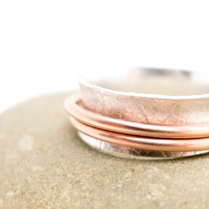 May include: A silver ring with a hammered texture and a copper band wrapped around it.
