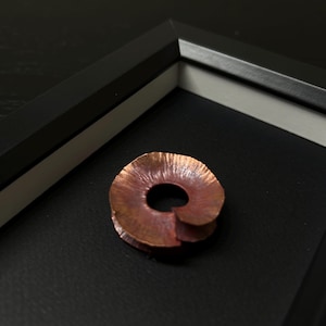 May include: A copper-coloured metal ring with a textured surface. The ring is displayed on a black background.