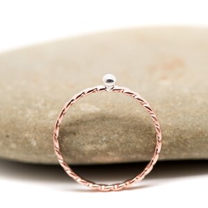 May include: A delicate silver ring with a twisted rose gold band and a small silver bead at the top.