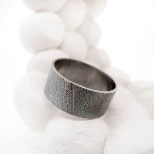 May include: A wide silver band ring with a textured leaf pattern.