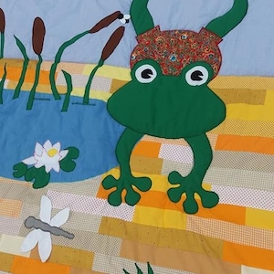 以下が含まれることがあります： 手作りのキルトで、気まぐれなカエルのデザインが特徴です。緑色のカエルは大きな目と模様の腹を持っています。キルトには、スイレン、ガマ、トンボのある池が含まれており、すべてパッチワークの背景に設定されています。