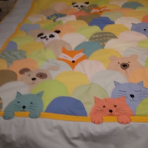 May include: A colorful quilt with a variety of animal faces peeking out from behind colorful, rounded shapes. The animals include a fox, a cat, a dog, a bear, and a panda.