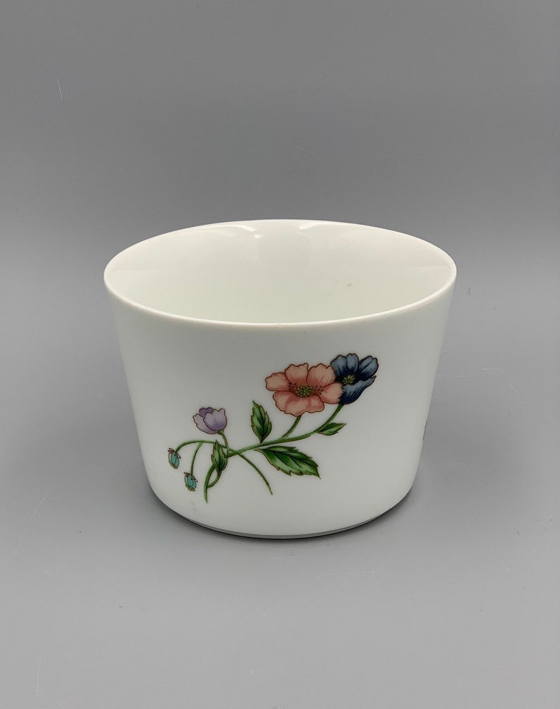 Puede incluir: Taza de cer&aacute;mica blanca con un dise&ntilde;o floral con flores rosas, azules y moradas con hojas verdes.