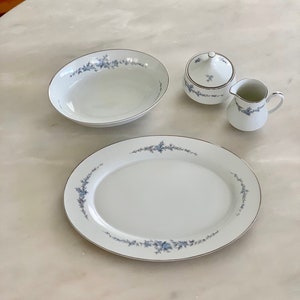 May include: A white oval platter with a blue floral design, a white bowl with a blue floral design, a white creamer with a blue floral design, and a white sugar bowl with a blue floral design and a lid.