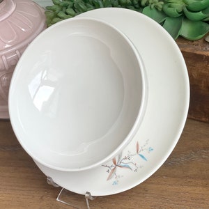 May include: A white ceramic bowl and plate set with a floral design in shades of blue, brown, and white.