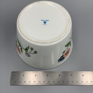 Puede incluir: Taz&oacute;n de porcelana blanca con un dise&ntilde;o floral con flores rosas, azules y verdes. El taz&oacute;n tiene un logotipo azul y blanco en la parte inferior que dice "House of Prill Porcelain".