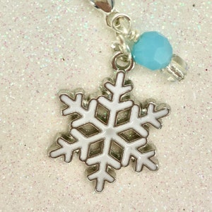 May include: A silver charm with a white snowflake and a light blue bead. The charm is attached to a silver lobster clasp.