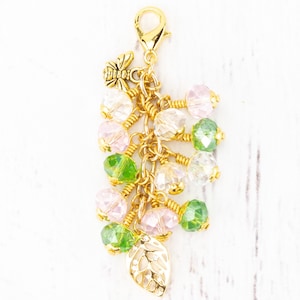 Puede incluir: Un charm dorado con un cierre de mosquet&oacute;n, un peque&ntilde;o charm de abeja y un grupo de cuentas. Las cuentas son en tonos rosa, verde y transparente, con un charm de hoja dorada en la parte inferior. Para pulsera o collar.
