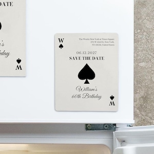 May include: Two rectangular magnets designed like playing cards with a cream background and black text. They feature a spade symbol, the date 06.12.2027, the text SAVE THE DATE, and William's 60th Birthday, along with the Westin New York address.