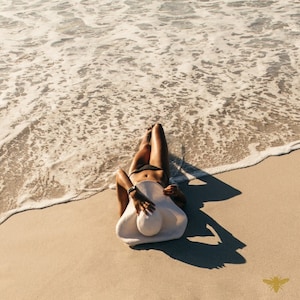 May include: A person wearing a black bikini lies on a sandy beach with a white sun hat. The person is facing the camera with their legs extended and their arms by their sides. The beach is covered in white sand and the ocean is in the background.