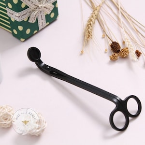May include: Black metal candle wick trimmer with a rounded tip and a pair of scissors. The tool is used to trim candle wicks.