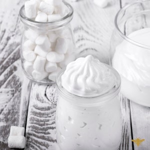 May include: Two glass jars filled with white marshmallows and whipped cream. The jars are on a white wooden surface.
