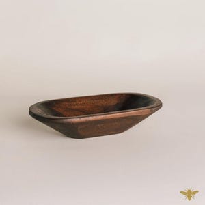 May include: A small, dark brown wooden bowl with an oval shape. The bowl has a smooth, polished finish and is empty. The bowl is likely used for decorative purposes or to hold small items.
