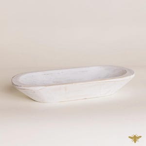 May include: A white, oval-shaped wooden bowl with a distressed finish. The bowl has a shallow depth and is ideal for decorative purposes or serving food. The wood grain is visible, adding to its rustic charm.