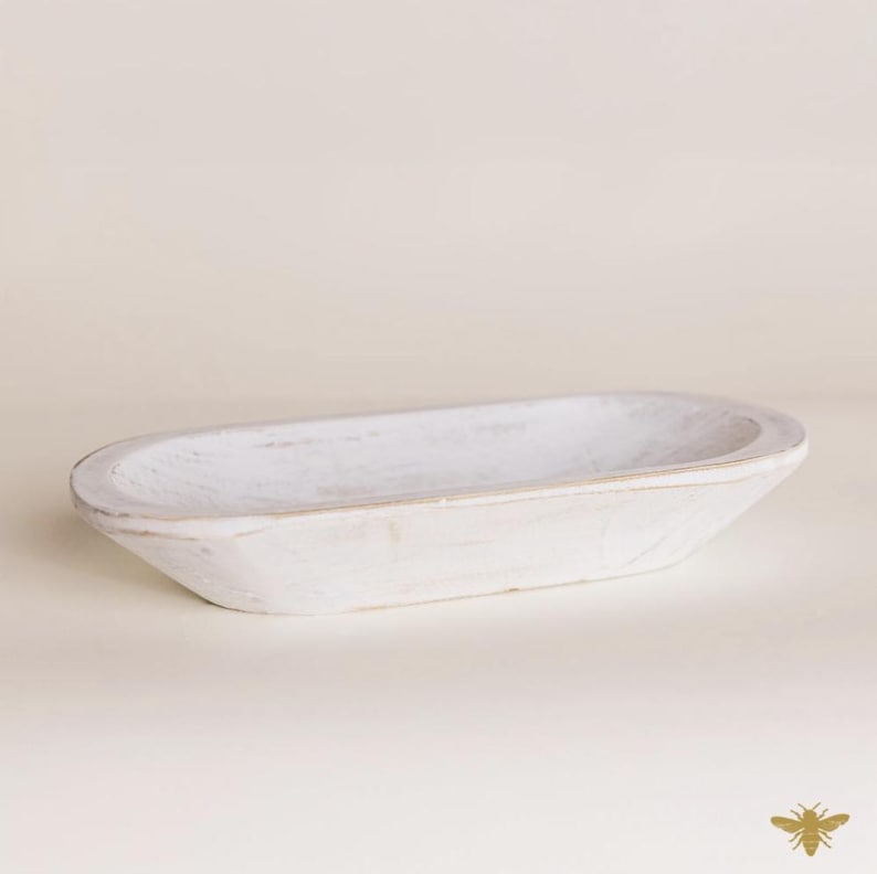 May include: A white, oval-shaped wooden bowl with a distressed finish. The bowl has a shallow depth and is ideal for decorative purposes or serving food. The wood grain is visible, adding to its rustic charm.