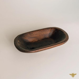 May include: A dark brown, oblong wooden bowl with rounded edges. The bowl has a smooth, polished finish and a deep interior. The wood grain is visible, adding texture and character to the piece. This decorative bowl is ideal for serving or display.