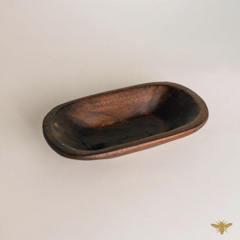 May include: A dark brown, oblong wooden bowl with rounded edges. The bowl has a smooth, polished finish and a deep interior. The wood grain is visible, adding texture and character to the piece. This decorative bowl is ideal for serving or display.