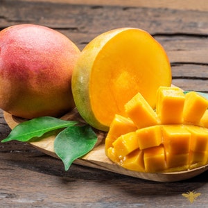 May include: Two ripe mangoes are displayed, one whole and one halved to show the vibrant orange flesh. The whole mango has red and yellow skin. Cubed mango pieces sit on a wooden board, with green leaves. The background is a rustic wooden surface.
