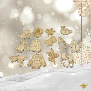 May include: A set of 15 wooden Christmas ornaments featuring winter-themed designs, including a snowman, a penguin, a mitten, a snowflake, a gingerbread man, a sweater, a hat, a cup of hot chocolate, and a sprig of holly.