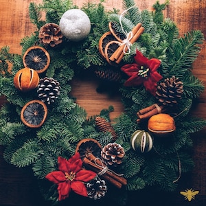 May include: A green Christmas wreath decorated with dried oranges, cinnamon sticks, pine cones, and a white ornament.