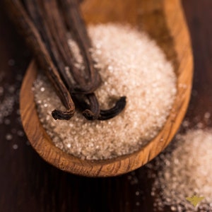 May include: A wooden bowl filled with brown sugar and vanilla beans. The vanilla beans are arranged in a fan shape and are partially submerged in the sugar.