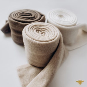 May include: Three rolls of soft, knitted fabric in beige, brown, and white. The fabric is rolled up and the ends are overlapping.