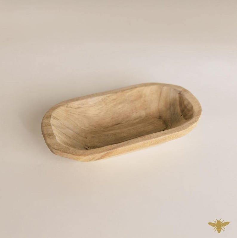 May include: A light-colored, wooden, oval-shaped bowl. The bowl has a smooth, natural finish and a shallow interior. The wood grain is visible, adding texture. The bowl is empty and sits on a neutral background.
