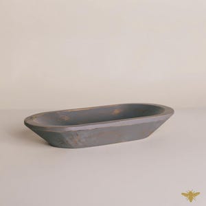May include: A gray, oval-shaped wooden bowl with a distressed finish. The bowl has a shallow depth and gently sloping sides. The exterior shows hints of gold undertones, adding a rustic charm. This decorative bowl is suitable for various home decor uses.