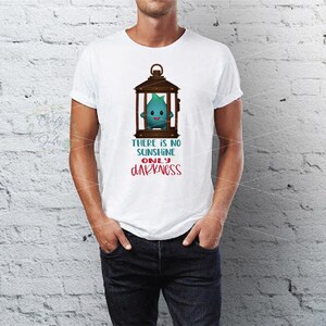Op de afbeelding: Wit T-shirt met een cartoonfiguur in een bruine lantaarn. Het turquoise karakter heeft een lachend gezicht. De tekst "THERE IS NO SUNSHINE ONLY DARKNESS" staat eronder in turquoise en rood.