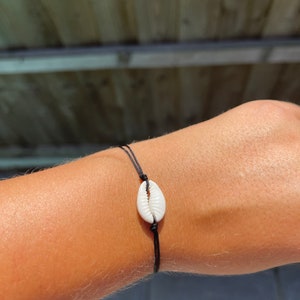 May include: A simple black string bracelet with a white seashell charm.