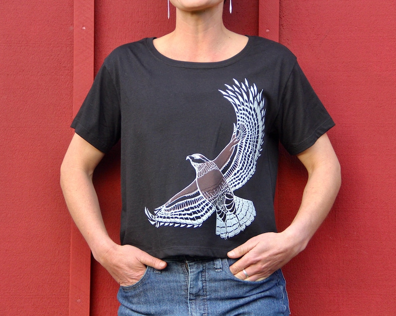May include: A black t-shirt with a white stylized image of a hawk in flight.