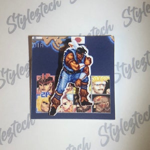 May include: A sticker featuring a pixelated character from a video game. The character is a man with brown hair and a blue shirt. He is standing in a fighting pose. The sticker is on a blue background with other pixelated characters in the background.
