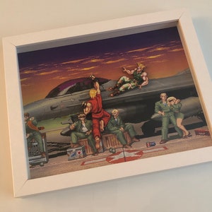 May include: A framed print of a pixelated image depicting a group of characters standing in front of a fighter jet against a sunset background. The characters are wearing various outfits, including a red jumpsuit, a green military uniform, and a blue shirt. The jet is gray and has a purple canopy.