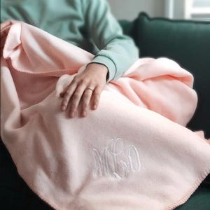 May include: A soft pink fleece blanket with a white embroidered monogram "MLO".