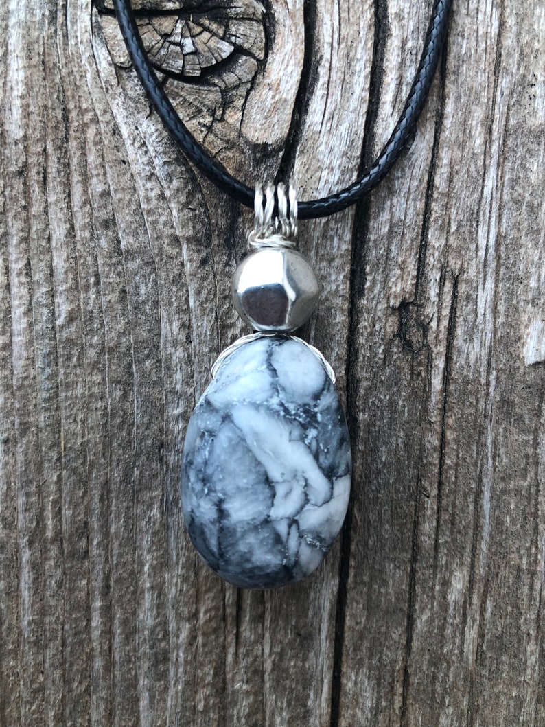 May include: A silver pendant necklace with a black cord. The pendant features a round silver bead and a teardrop-shaped grey and white stone.