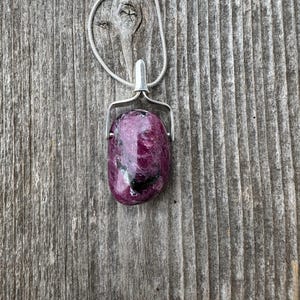May include: A silver chain necklace with a pendant featuring a pink and black gemstone. The gemstone is set in a silver bezel and hangs from a silver bail.