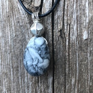May include: A silver pendant necklace with a black cord. The pendant features a white and grey marbled stone with a silver bead above it.
