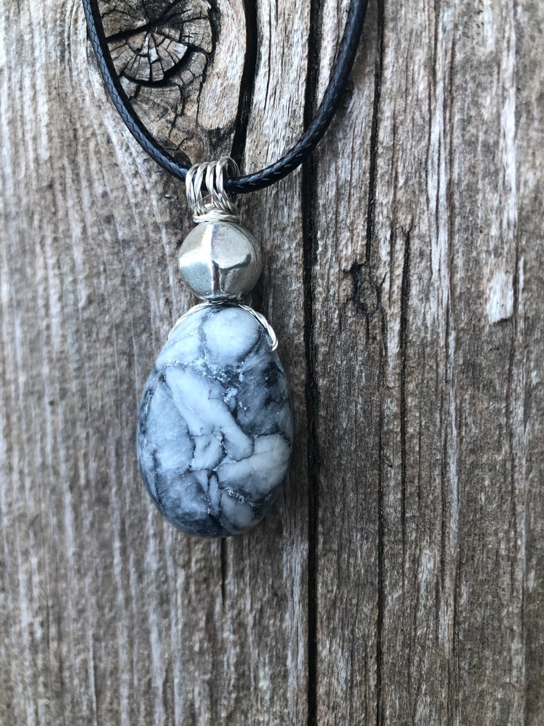 May include: A silver pendant necklace with a black cord. The pendant features a white and grey marbled stone with a silver bead above it.