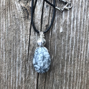 May include: A black leather cord necklace with a silver pendant featuring a white and grey marbled stone.