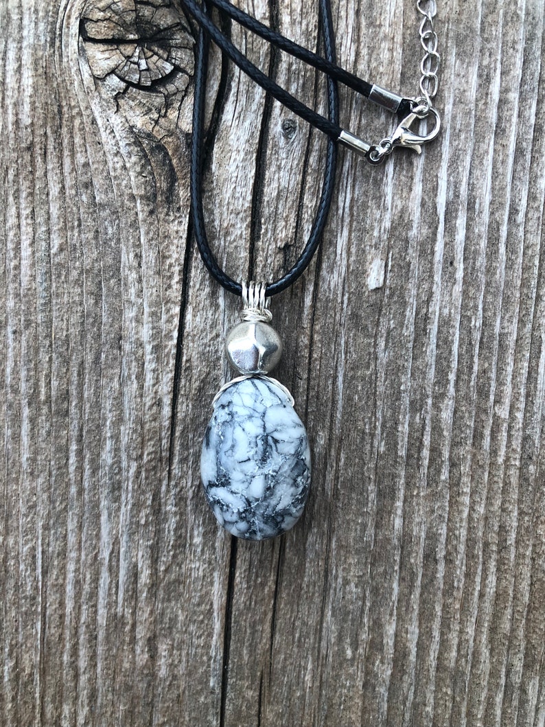 May include: A black leather cord necklace with a silver pendant featuring a white and grey marbled stone.
