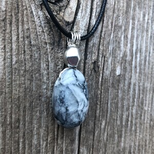 May include: A black cord necklace with a silver pendant featuring a white and grey marbled stone.
