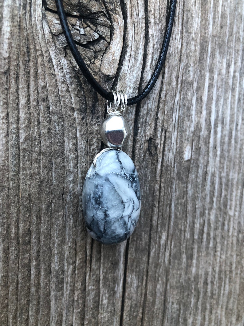 May include: A black cord necklace with a silver pendant featuring a white and grey marbled stone.