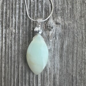 Può includere: Una collana con catena d'argento con un ciondolo a forma di lacrima verde chiaro. Il ciondolo è avvolto in filo d'argento.