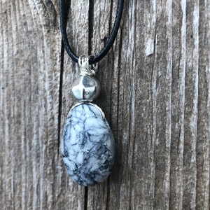 May include: A silver wire-wrapped pendant necklace with a black and white marbled stone and a silver bead. The necklace is on a black cord.