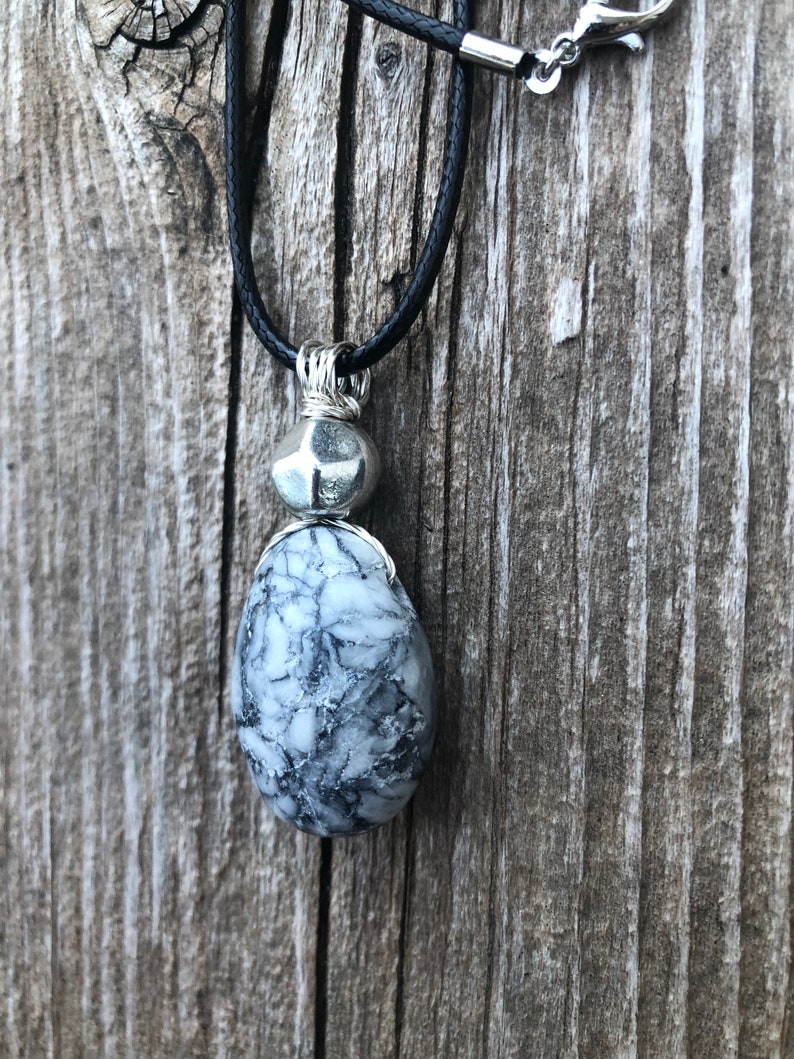 May include: A silver wire-wrapped pendant necklace with a black and white marbled stone and a silver bead. The necklace is on a black cord.