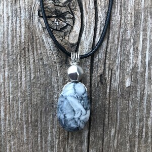 May include: A silver pendant necklace with a black cord. The pendant features a white and grey stone with a silver bead.