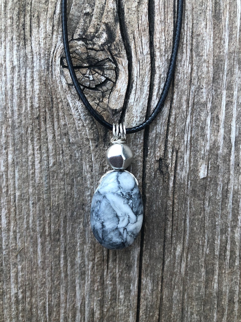 May include: A silver pendant necklace with a black cord. The pendant features a white and grey stone with a silver bead.