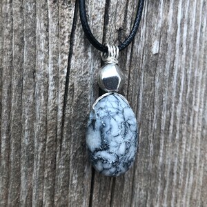 May include: A black leather cord necklace with a silver pendant featuring a white and grey stone. The stone has a unique marbled pattern.